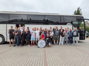 Grupa osób machających przed białym autokarem, z bębnem z napisem Brzeźno na pierwszym planie