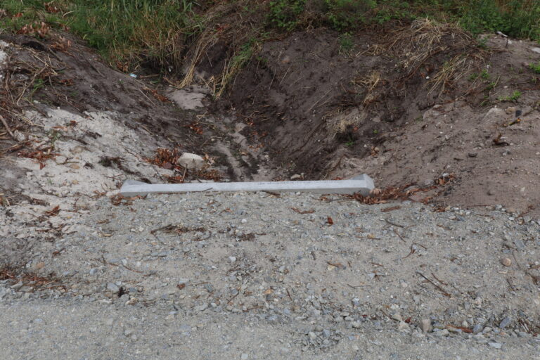 Betonowy element odwodnienia zamontowany na krawędzi żwirowej drogi przy ziemnym rowie