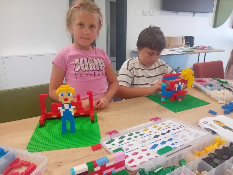 Dwoje dzieci budujących kolorowe figurki z klocków LEGO przy stole