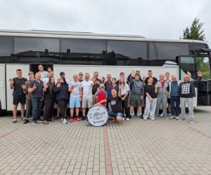 Grupa osób machających przed białym autokarem, z bębnem z napisem Brzeźno na pierwszym planie